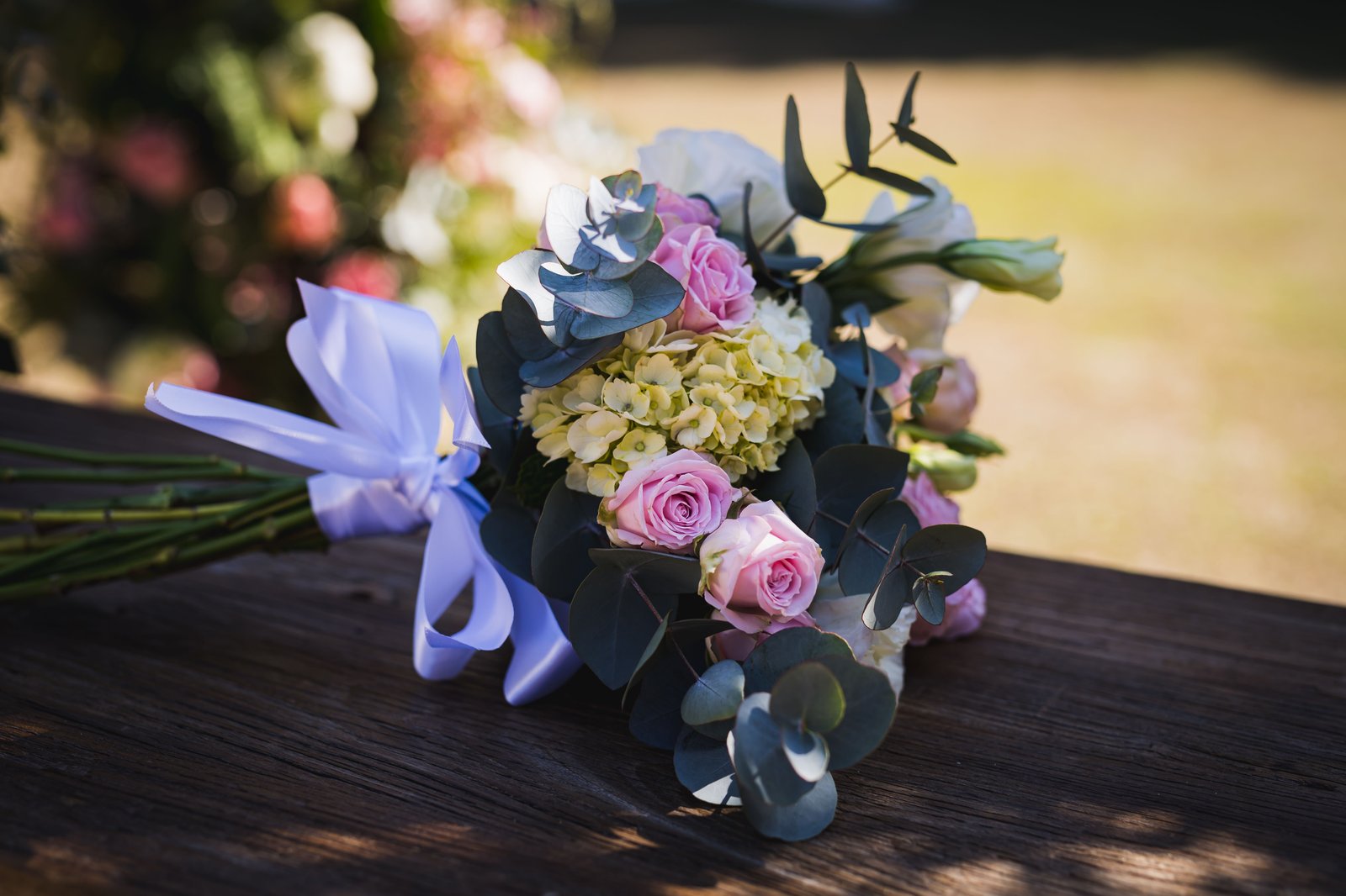 A bouquet of pink roses, yellow hydrangeas, and eucalyptus rests on a wooden surface.